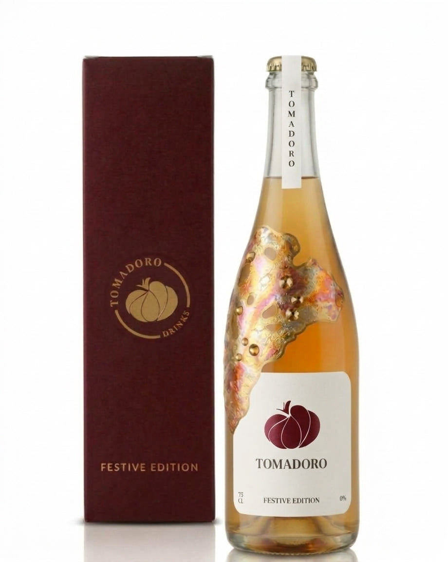 Tomadoro Festive Edition by artist Mart Krijger: alcohol-free sparkling tomato drink in a 75 cl bottle decorated with gold leaf and Swarovski crystals, next to a burgundy gift box with a gold logo.